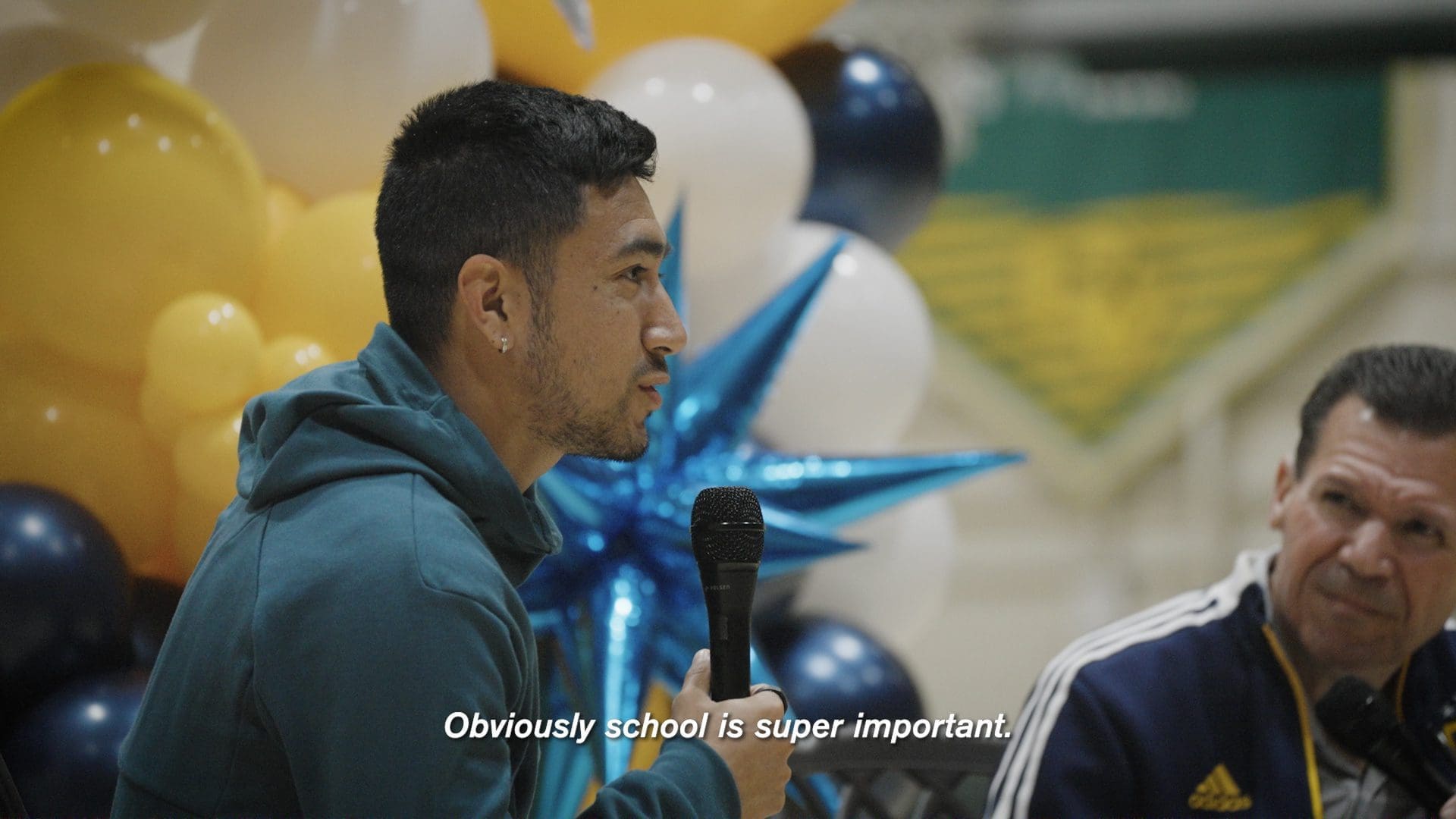 RIOT, NYC Creative Agency: LA Galaxy’s Memo Rodriguez speaking into a microphone at a community event during Galaxy Rise, surrounded by balloons and students LA Galaxy’s Memo Rodriguez speaking into a microphone at a community event during Galaxy Rise, surrounded by balloons and students