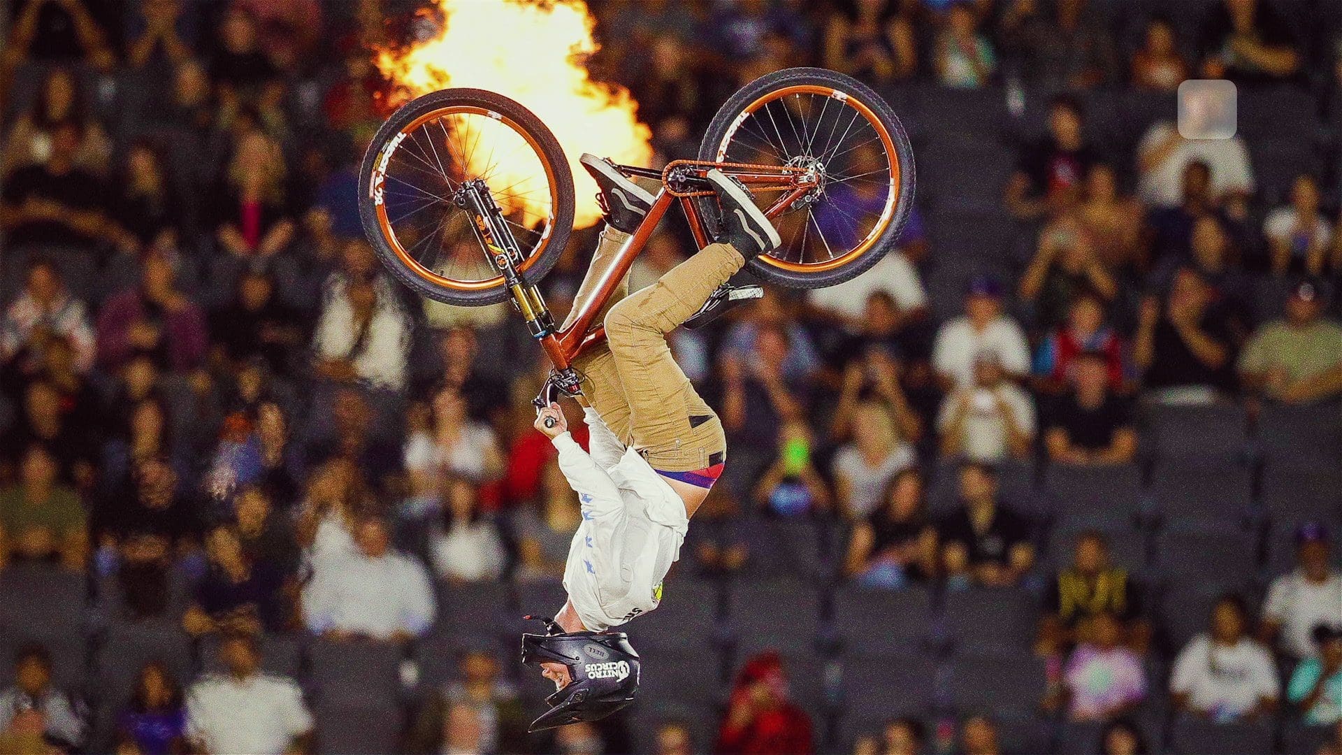 BMX rider performing a backflip with flames in the background at Dignity Health Sports Park.