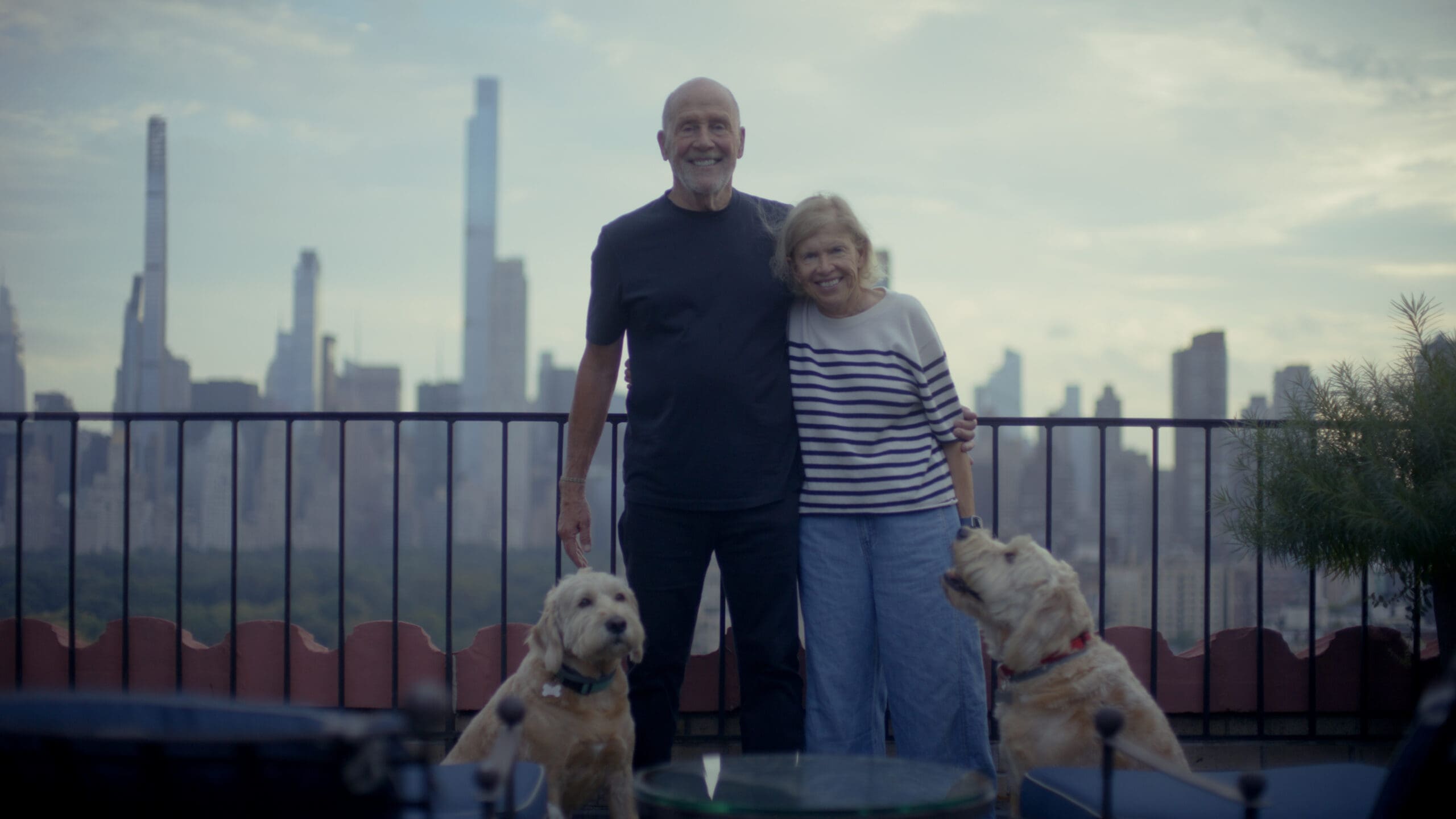 Lew Frankfort standing with his wife Bobbi Frankfort and their two dogs on their terrace overlooking New York City, from the Bag Man film by RIOT for Coach.