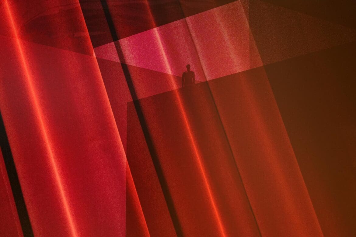 Surreal artwork inspired by David Lynch, featuring a silhouetted figure amidst layered red curtains and geometric light patterns.