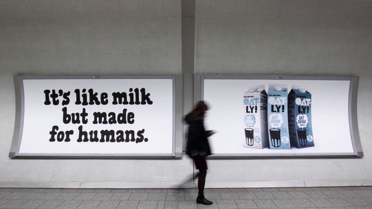 Oatly subway ad showing the slogan “It’s like milk but made for humans” alongside product cartons, with a passerby walking past the posters.