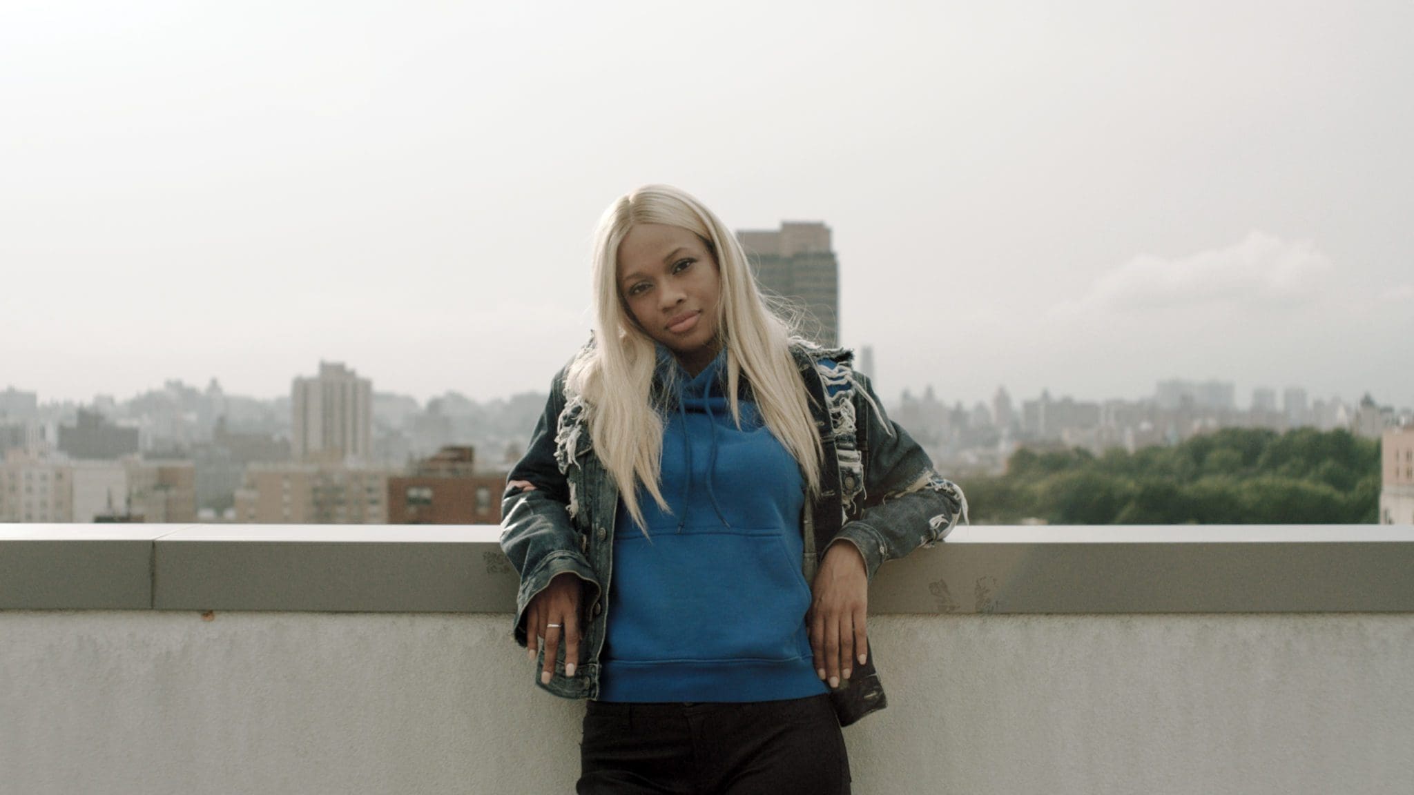 RIOT, NYC Creative Agency: Fatima B standing on a rooftop in New York City, wearing a blue hoodie and denim jacket, from the Reebok Take A Walk series. Fatima B standing on a rooftop in New York City, wearing a blue hoodie and denim jacket, from the Reebok Take A Walk series.
