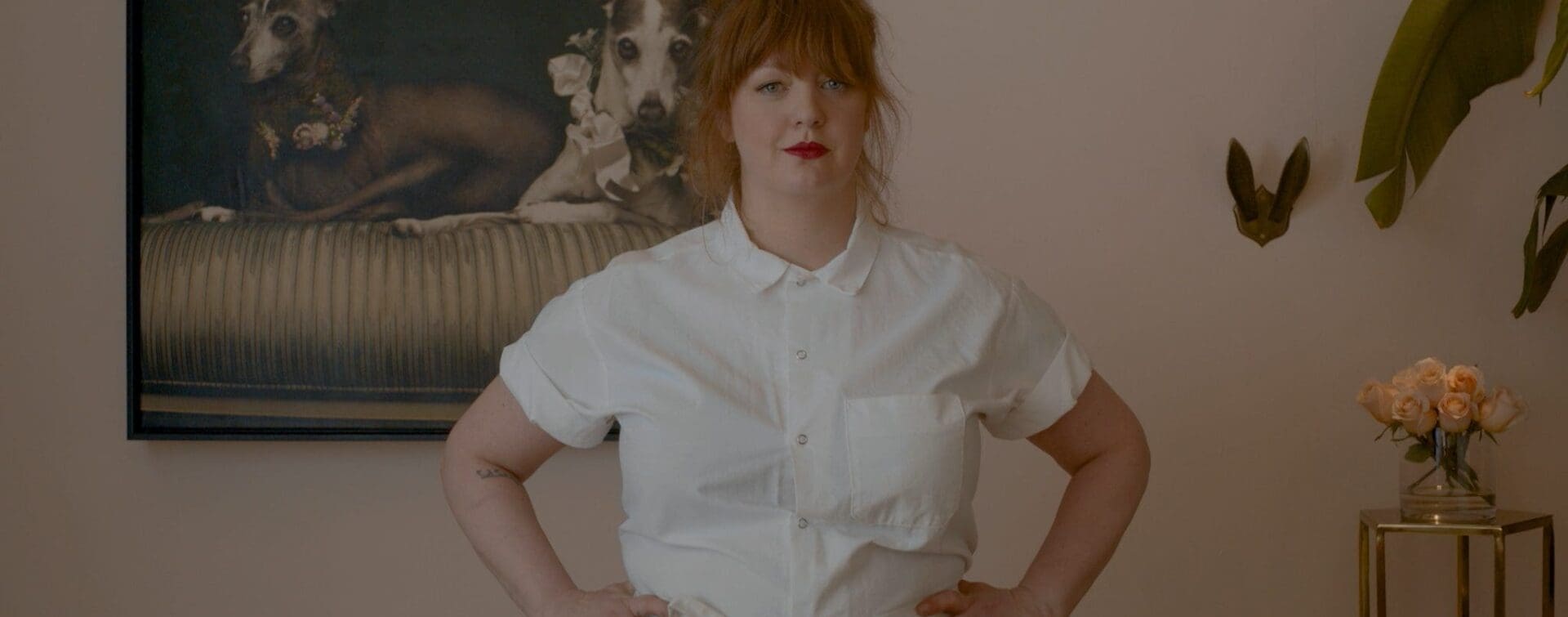 Jamie Malone with Her Dogs – A Glimpse Into Her World Chef Jamie Malone standing in front of a framed portrait of her beloved dogs, showcasing her connection to home and her personal life.
