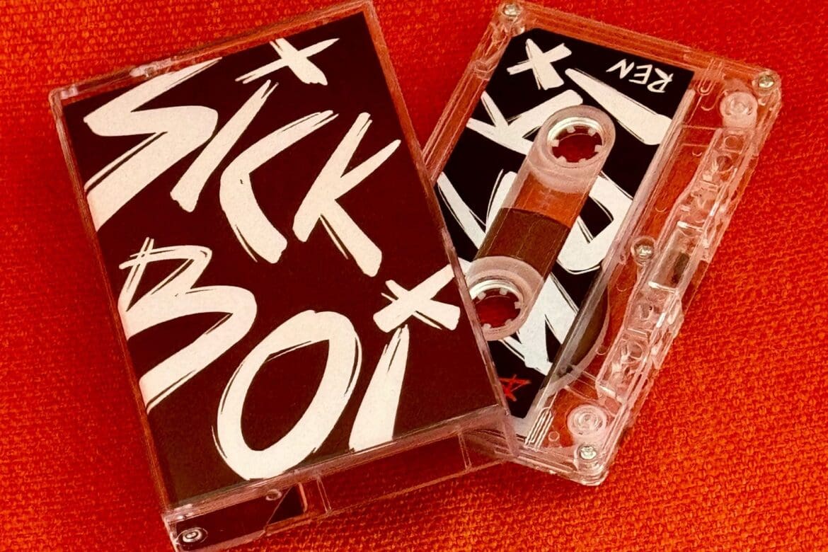 Cassette tape of Ren's 'Sick Boi' album with bold lettering on the cover, placed against a vibrant orange background.