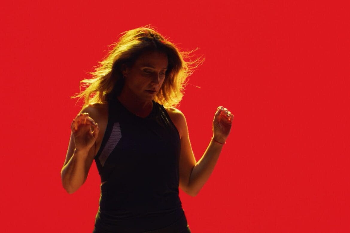 Laurie Cole captured mid-motion against a bold red backdrop, embodying strength, rhythm, and resilience during the SoulCycle docufilm series.