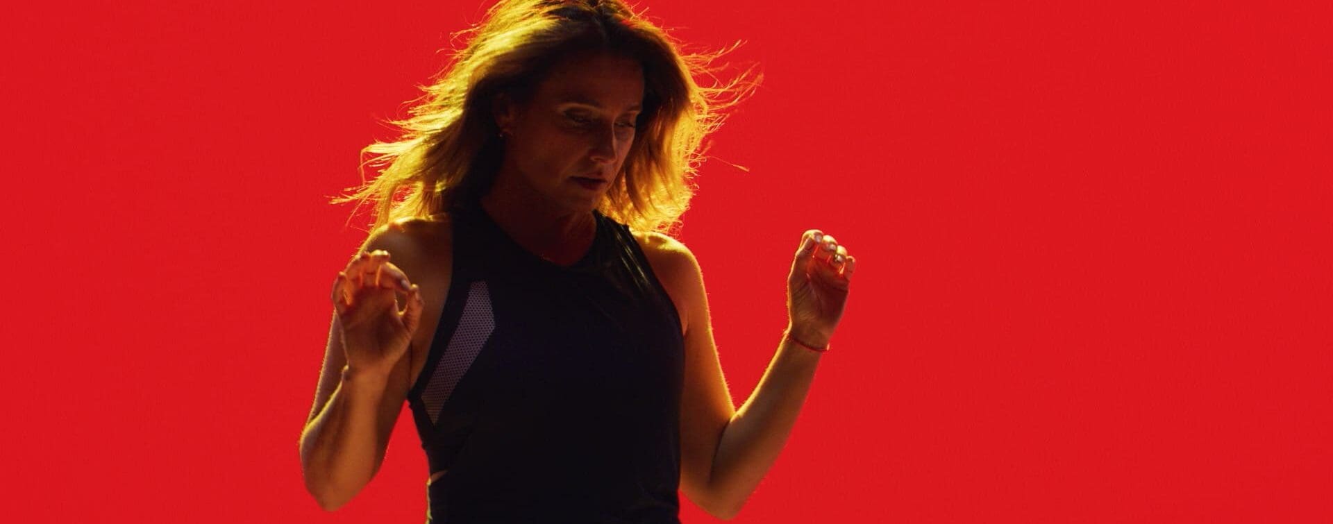 Laurie Cole in Motion – SoulCycle DocuFilm Still Laurie Cole captured mid-motion against a bold red backdrop, embodying strength, rhythm, and resilience during the SoulCycle docufilm series.