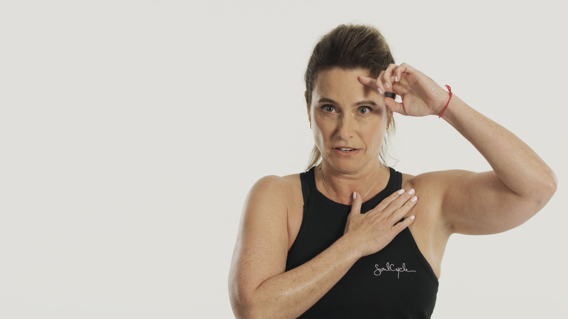 RIOT, NYC Creative Agency: Laurie Cole placing her hand on her chest in a thoughtful studio portrait, showcasing strength and authenticity during the SoulCycle docufilm series. Laurie Cole placing her hand on her chest in a thoughtful studio portrait, showcasing strength and authenticity during the SoulCycle docufilm series.