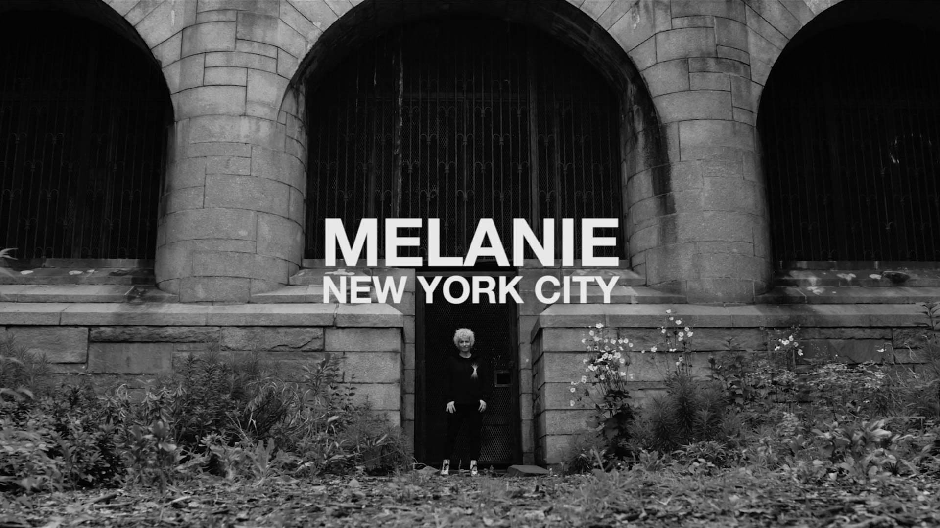Melanie standing in front of a gothic stone building in New York City, representing her roots and strength as a SoulCycle instructor.
