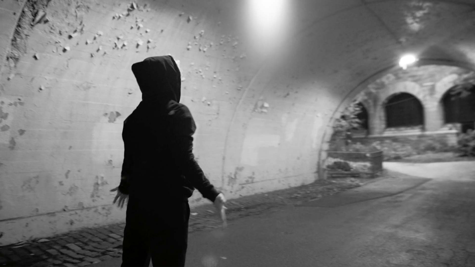 RIOT, NYC Creative Agency: Melanie standing in a dark tunnel in New York City, wearing a hoodie and looking upwards, symbolizing resilience and introspection. Melanie standing in a dark tunnel in New York City, wearing a hoodie and looking upwards, symbolizing resilience and introspection.