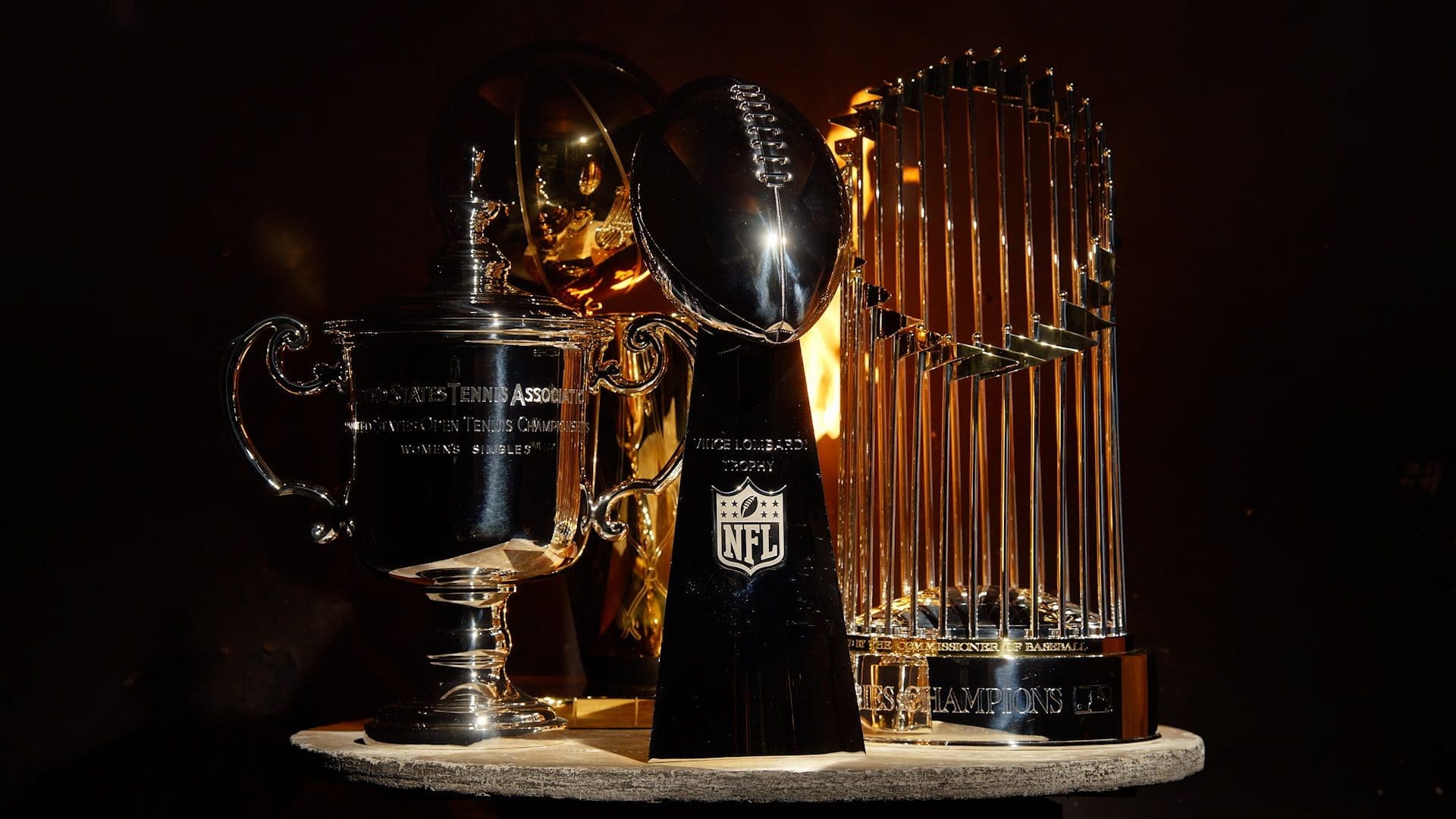 RIOT, NYC Creative Agency: An array of prestigious sports trophies including the USTA Women's Singles trophy, the NFL's Vince Lombardi Trophy, and the MLB's Commissioner's Trophy, all crafted by Tiffany & Co., displayed against a dark background. An array of prestigious sports trophies including the USTA Women's Singles trophy, the NFL's Vince Lombardi Trophy, and the MLB's Commissioner's Trophy, all crafted by Tiffany & Co., displayed against a dark background.