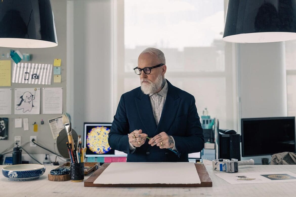Christopher Young standing over a blank page, surrounded by brushes and creative tools