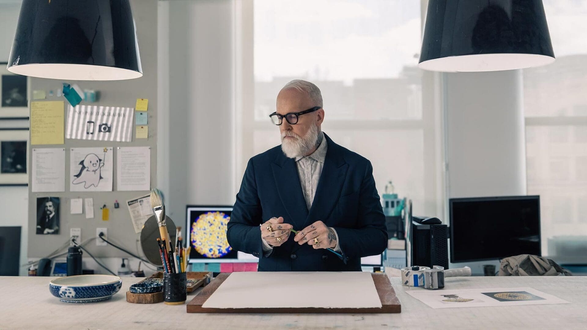 Christopher Young standing over a blank page, surrounded by brushes and creative tools