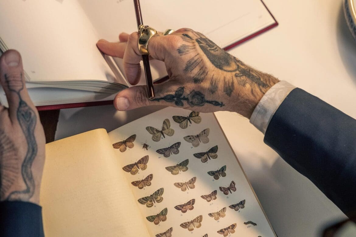 Close-up of Christopher Young’s tattooed hands flipping through a reference book of butterflies