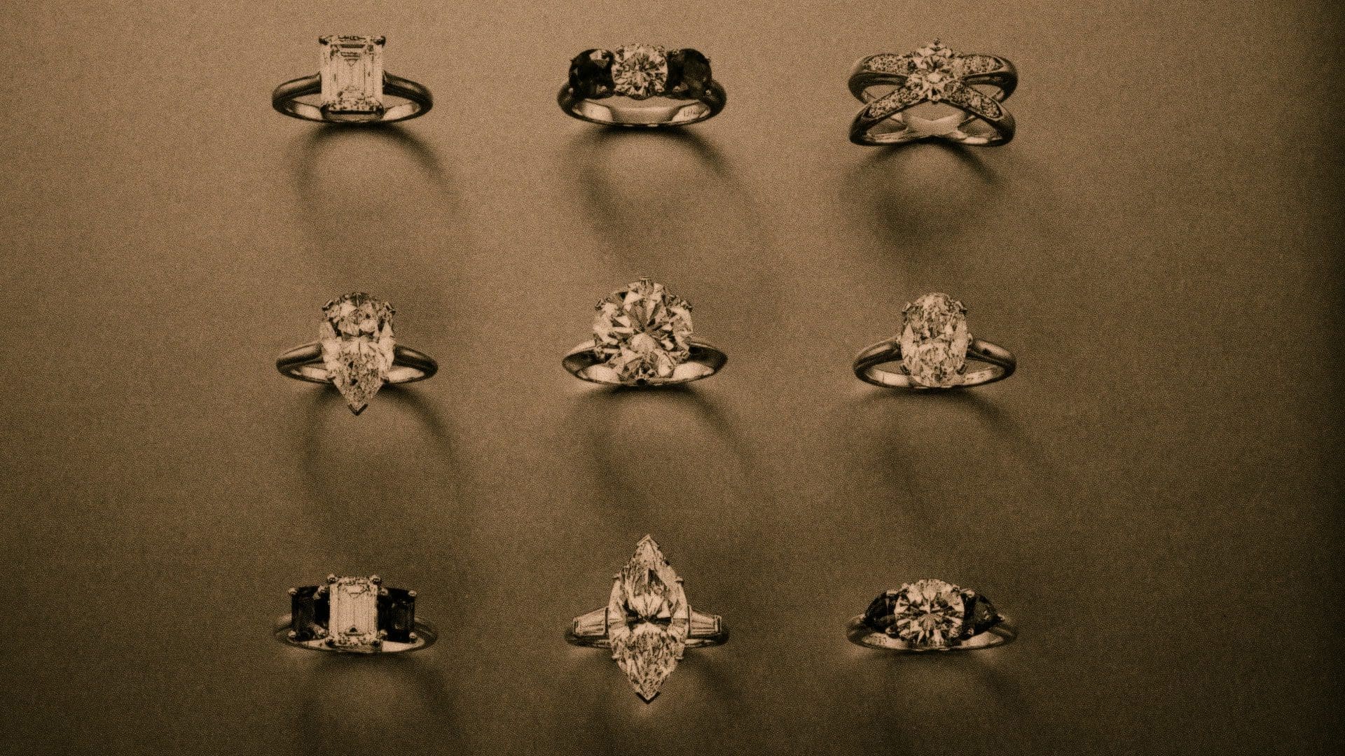 RIOT, NYC Creative Agency: Sepia-toned image displaying a selection of nine Tiffany & Co. engagement rings, each featuring the revolutionary Tiffany setting that elevated diamond jewelry design, against a dark backdrop. Sepia-toned image displaying a selection of nine Tiffany & Co. engagement rings, each featuring the revolutionary Tiffany setting that elevated diamond jewelry design, against a dark backdrop.