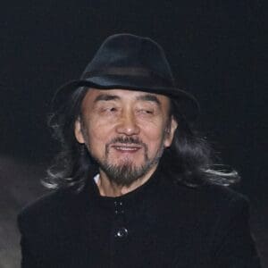 Yohji Yamamoto wearing a black hat and black coat, smiling as he receives applause at the end of his Fall/Winter 2010 Y-3 show during New York Fashion Week.