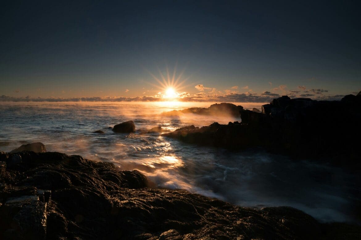 Sunrise over ocean waves crashing against a rocky shoreline
