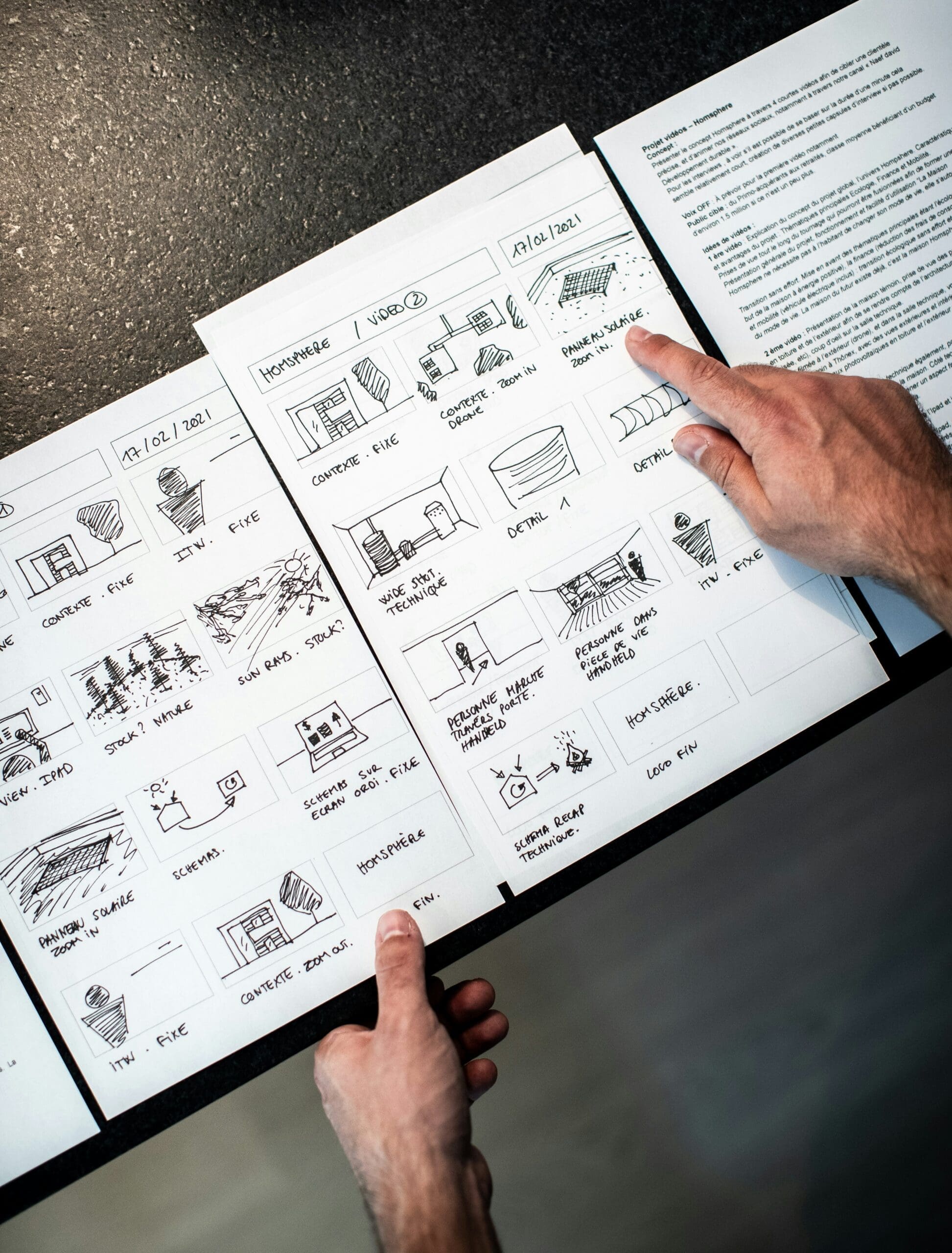 Close-up of hands reviewing a detailed storyboard for a video production project, showing sketches and scene descriptions.