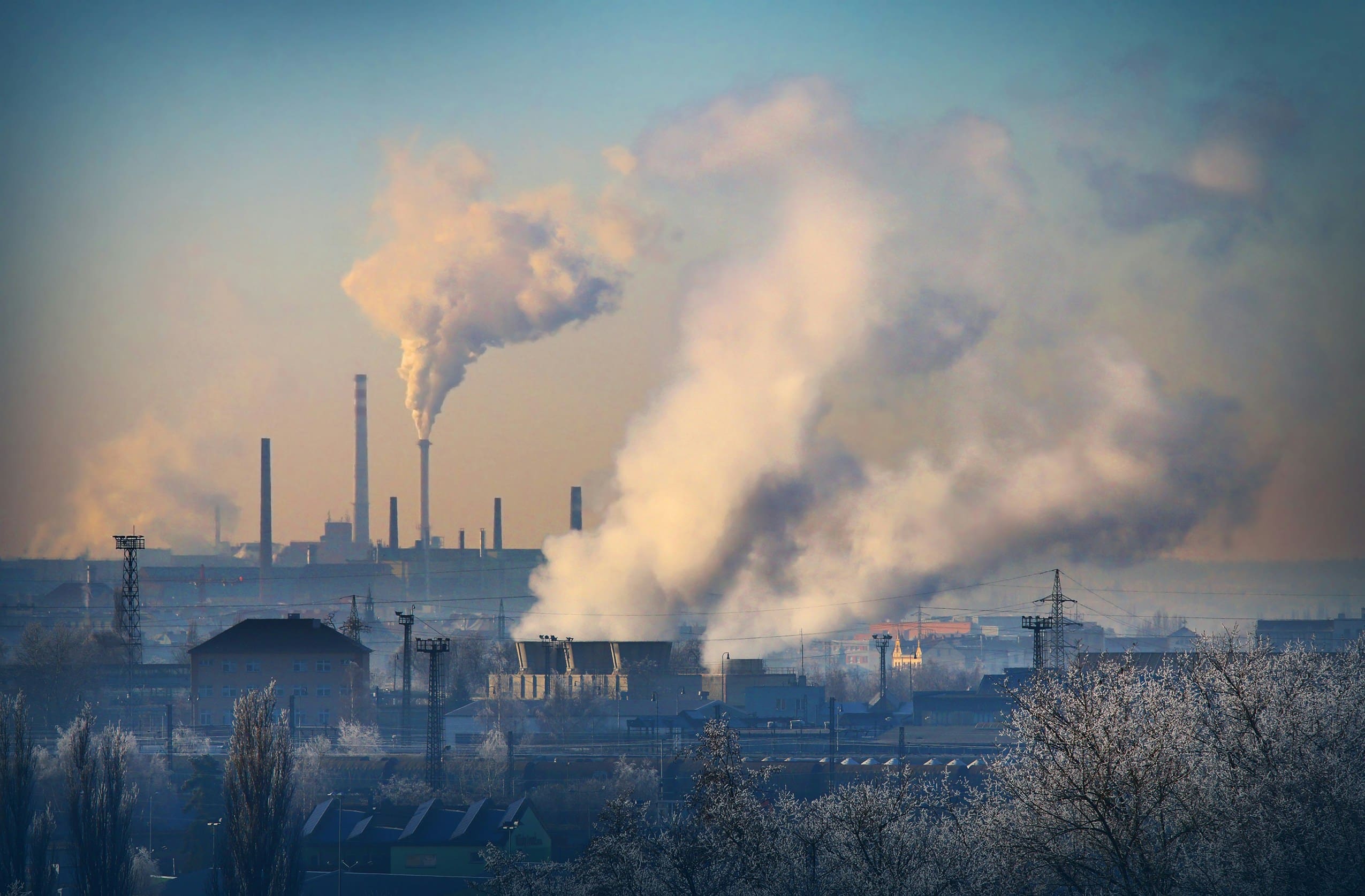 Thick smoke rising from factories near a residential area under a hazy sky
