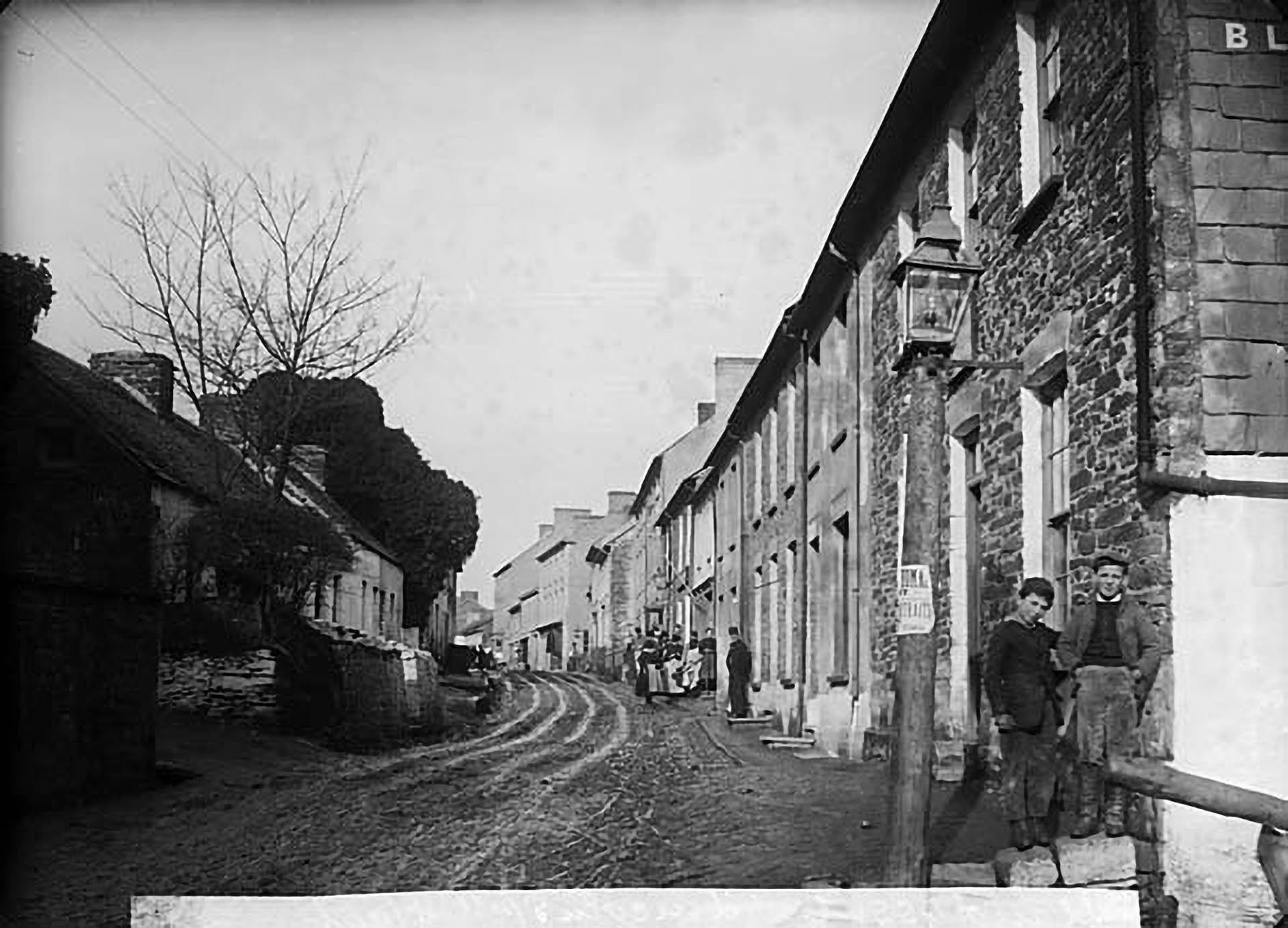 A black and white photograph of Lincoln Street in Llandysul, Wales, showing a historical view of the street with stone houses and people standing outside.