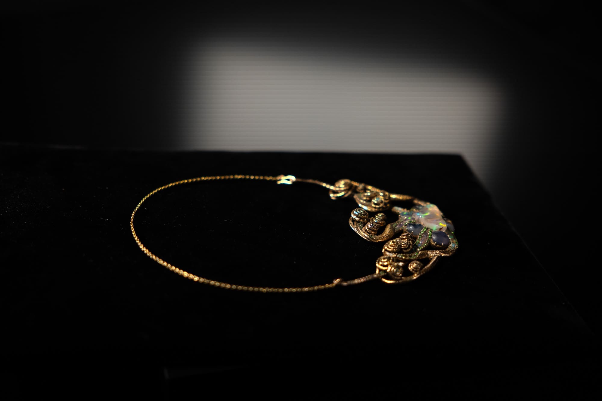 The Medusa pendant by Louis Comfort Tiffany, resting on black velvet, its opals flickering under soft light.