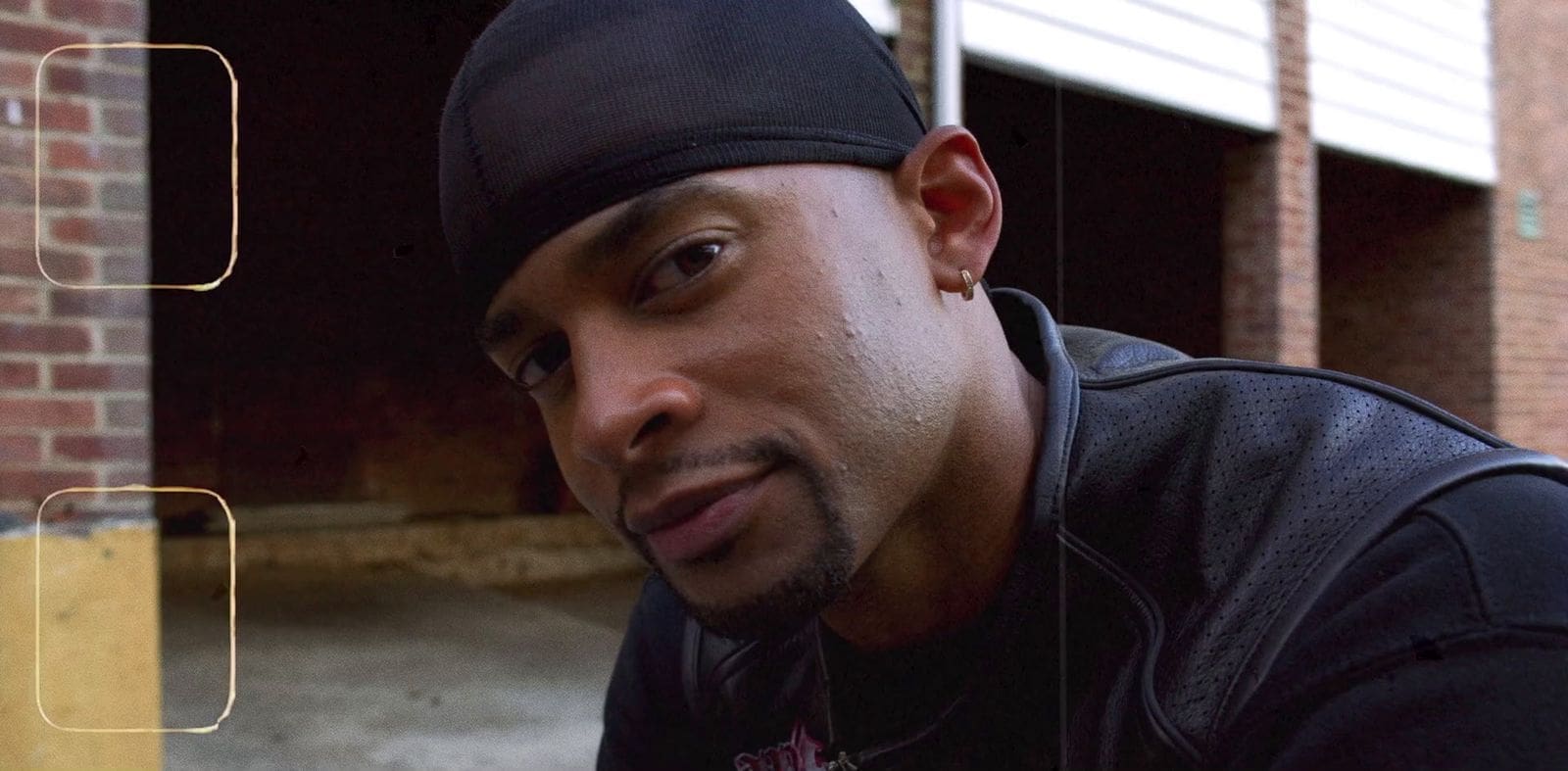 Close-up of Mike Press wearing a black durag and leather jacket, exuding confidence in an urban setting.