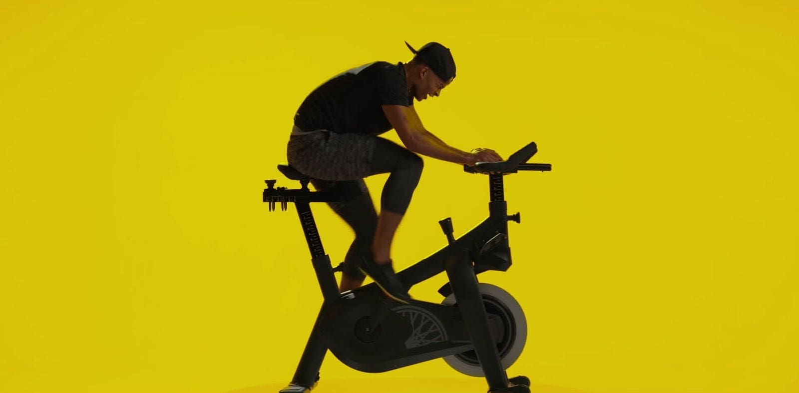 Mike Press riding a SoulCycle bike in a dynamic pose, set against a bold yellow background.