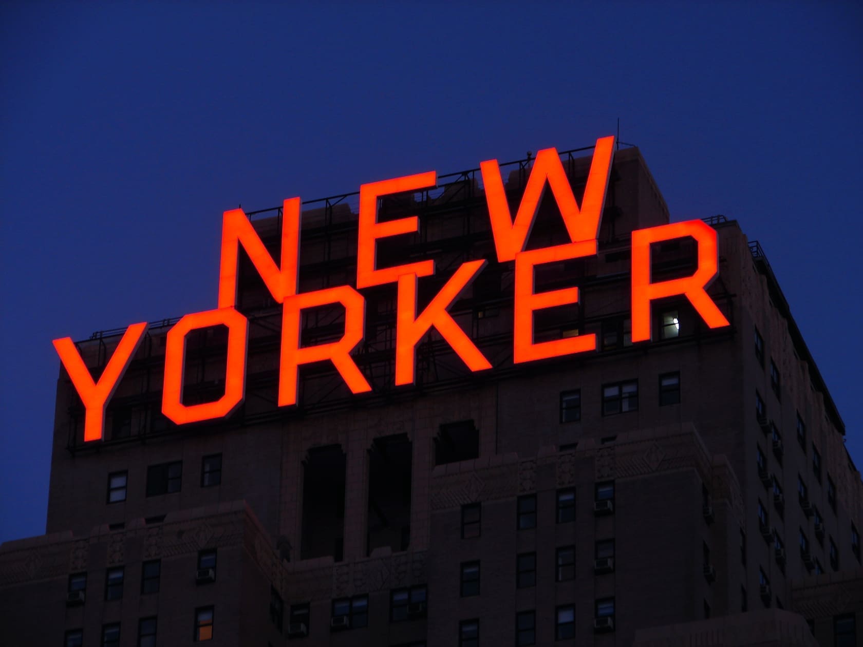 The iconic red neon sign of the New Yorker Hotel illuminated against the night sky.