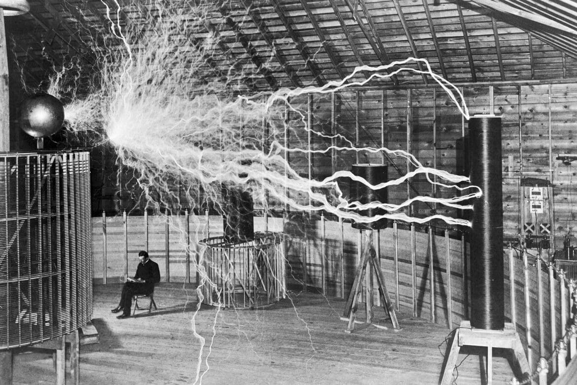 Nikola Tesla sitting in his laboratory surrounded by electrical sparks from his equipment.