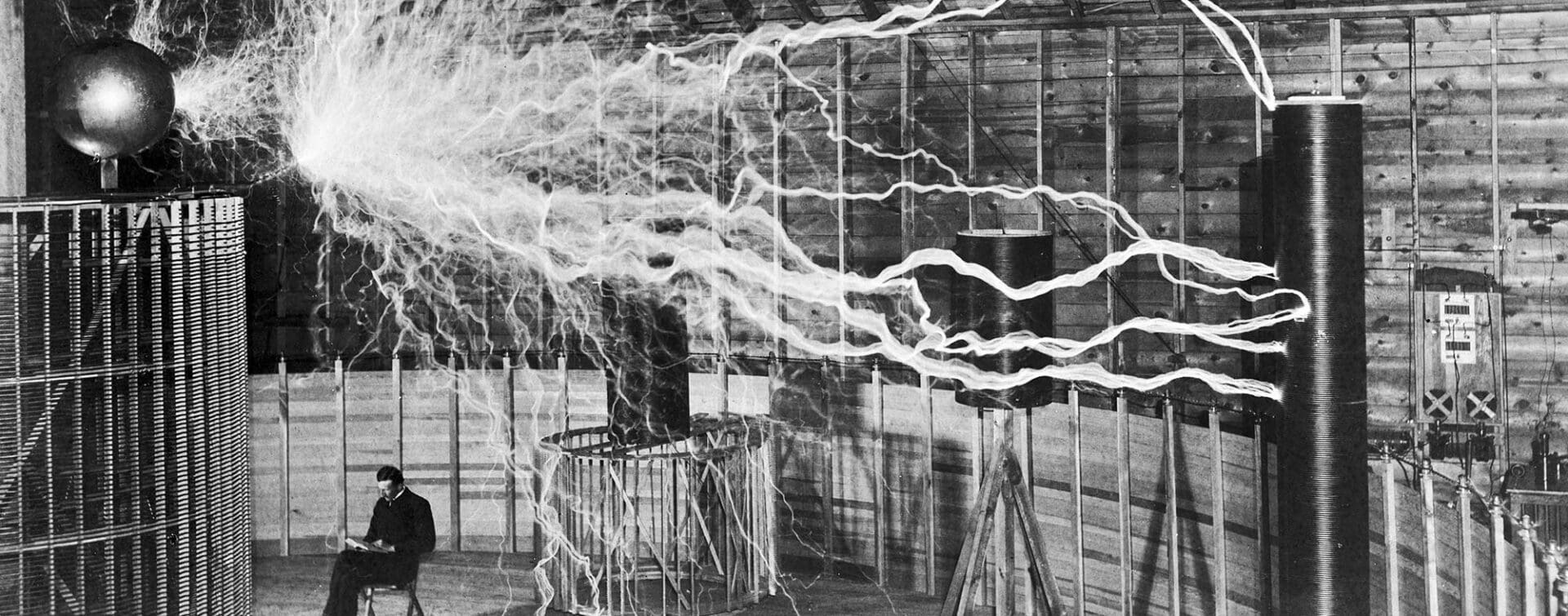 Nikola Tesla sitting in his laboratory surrounded by electrical sparks from his equipment.