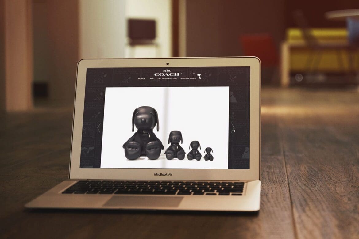 A laptop screen displaying the Coach x Peanuts collaboration with black Snoopy figurines featured on the website.