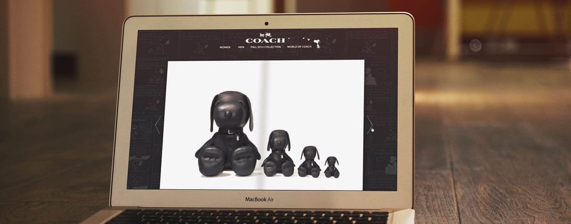A laptop screen displaying the Coach x Peanuts collaboration with black Snoopy figurines featured on the website.
