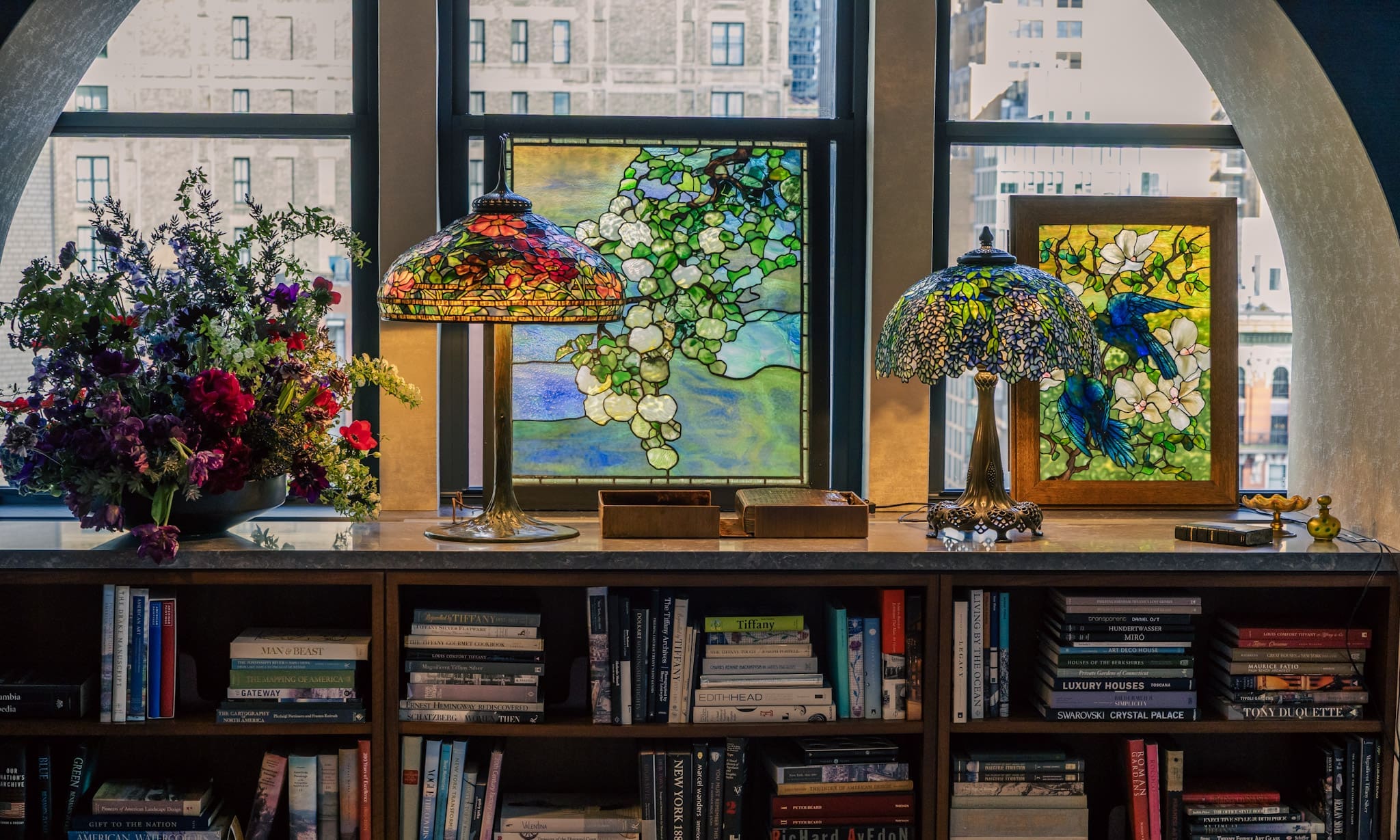 Tiffany stained glass and lamps on a bookshelf by a window, staged inside Tiffany HQ and photographed by RIOT.